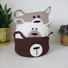 three crocheted stuffed animals sitting in a basket next to some potted plants