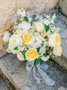 a bridal bouquet sitting on the steps next to a stone wall with white and yellow flowers