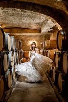 a woman in a white dress is standing among wine barrels