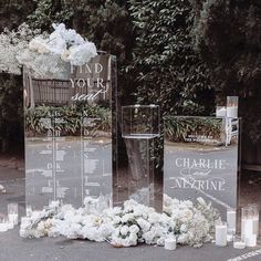 an arrangement of flowers and candles are on the ground next to two clear acrylic signs