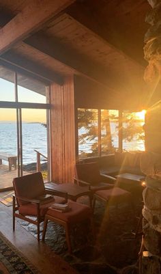 a living room with large windows overlooking the water at sunset or sunrise, and two chairs facing each other