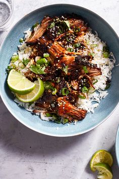 a blue bowl filled with rice and meat on top of a white table next to lime wedges