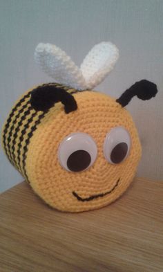 a crocheted toy with eyes and a bee's head on top of a wooden table