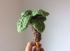 a crocheted palm tree is held up by a person's hand with a pencil