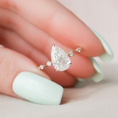 a woman's hand holding a ring with a pear shaped diamond on top of it