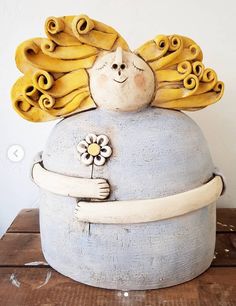 a ceramic sculpture of a woman with yellow hair and flowers on her head, sitting on a wooden table