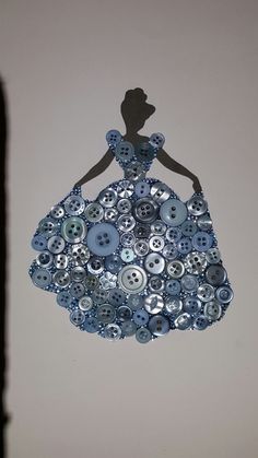 a woman in a blue dress made out of buttons on a white wall with a black shadow