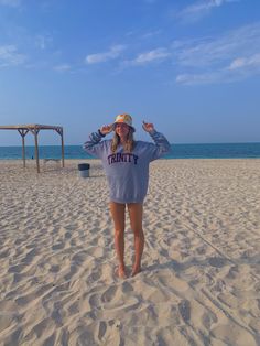 a woman standing on top of a sandy beach next to the ocean with her hands behind her head