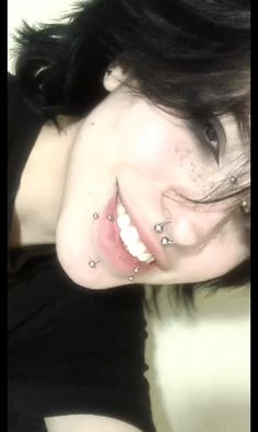 a woman with black hair and piercings on her face smiles at the camera while wearing a black shirt