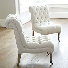 two white tufted chairs sitting on top of a hard wood floor next to a window