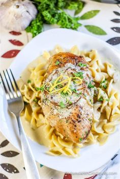 chicken breast with lemon sauce and pasta on a white plate next to a knife and fork