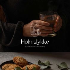 a person holding a glass and some food on a table with the words homskyke above it