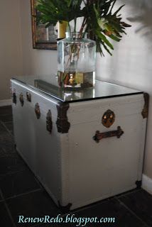 a white trunk with a plant on top and a mirror above it in a room