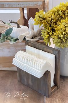 a vase filled with yellow flowers sitting on top of a wooden table next to a stack of napkins