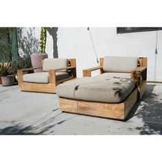 two wooden lounge chairs sitting next to each other on a cement ground near a building