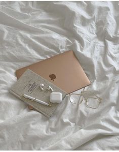 an apple laptop computer sitting on top of a bed next to headphones and glasses