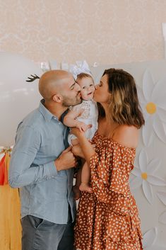 a man and woman holding a baby in front of a wall with flowers on it