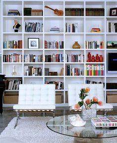 a living room filled with lots of white furniture and bookshelves full of books