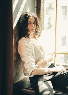 a woman sitting on a window sill in front of a window with sunlight coming through