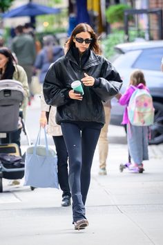 a woman in black jacket and leggings walking down the street