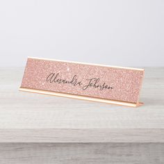 a pink glitter name plate on top of a wooden table