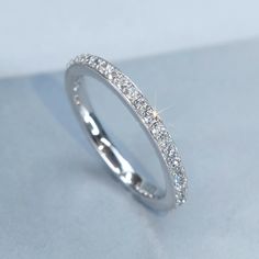 a white gold ring with small diamonds on the inside and outside, sitting on a light blue surface