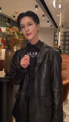 a woman wearing glasses and a black leather jacket with the word glam printed on it