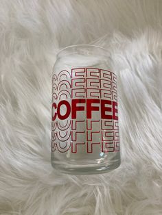 a glass with the word coffee on it sitting on a white fur covered surface,