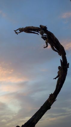 two people climbing up a tree branch in the air at sunset or dawn with clouds behind them