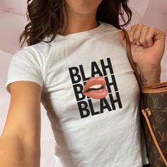 Make a bold statement with this eye-catching "Blah Blah Blah" design. The graphic features the words "BLAH BLAH BLAH" in large, bold black letters, overlaid with a close-up of vibrant, glossy lips. This playful and sassy design is perfect for those who love to express themselves with style and a touch of attitude. **Tee Details - **Brand Gildan - **Model Women's Baby Tee - **Material 100% preshrunk cotton - **Features    - Soft and comfortable fit, tailored for a feminine silhouette   - Classic Cute Graphic Design Tops For Streetwear, Cute Graphic Tops For Streetwear, Fitted Fun Graphic T-shirt, White Pop Culture Tops With Slogan, White Pop Culture Slogan Tops, White Pop Culture Slogan Top, Fitted Pop Culture T-shirt With Letter Print, Fun Fitted Shirt With Graphic Print, Unisex Trendy Streetwear Tops