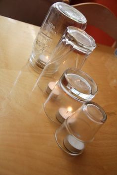 three clear cups sitting on top of a wooden table next to each other with candles in them