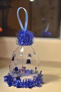 an ornament shaped like a bell with blue tinsel around it and stars on the bottom