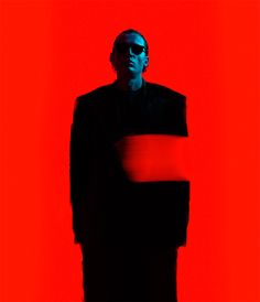 a man in a black suit and sunglasses standing against a red background with his hands on his hips