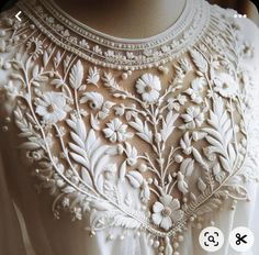 a white dress with flowers and pearls on it's neckline is seen in this image