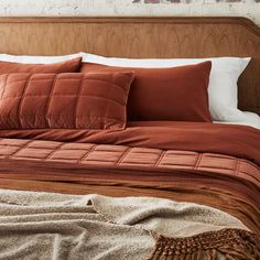 a bed with red pillows and blankets on top of it next to a brick wall