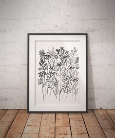 a black and white drawing of flowers in a frame on a wooden floor next to a brick wall