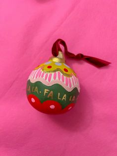 an ornament on a pink surface with a red ribbon hanging from it's end