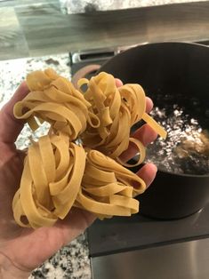 a person holding up some noodles in front of a frying pan on the stove