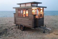 a tiny house sitting on top of a sandy beach next to the ocean at dusk