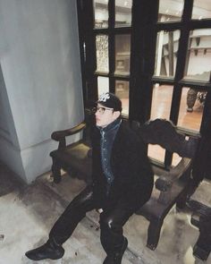 a man sitting on top of a wooden bench next to a tall window with glass panes