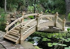 a wooden bridge over a small pond with lily pads and water lilies in the background