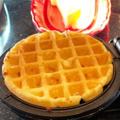 a waffle sitting on top of a black plate next to a red vase with an apple in it