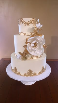 a three tiered white and gold wedding cake with flowers on it's side