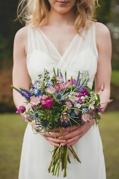 a woman in a white dress holding a bouquet of purple and blue flowers on her wedding day