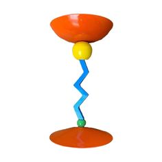 an orange and blue object is hanging on a white wall, with one yellow ball in the air