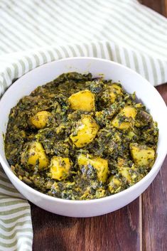 a white bowl filled with spinach and potatoes on top of a wooden table next to a striped towel