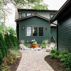 a brick walkway leads to a green house with white chairs and trees in the background