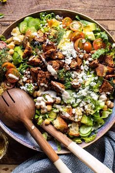 a salad with chicken, lettuce and tomatoes in a bowl next to a wooden spoon