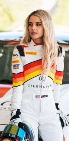 a woman standing next to a racing car wearing a rainbow colored outfit and holding a helmet