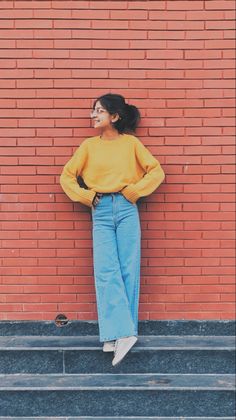 a woman leaning against a brick wall with her hands on her hips and looking up